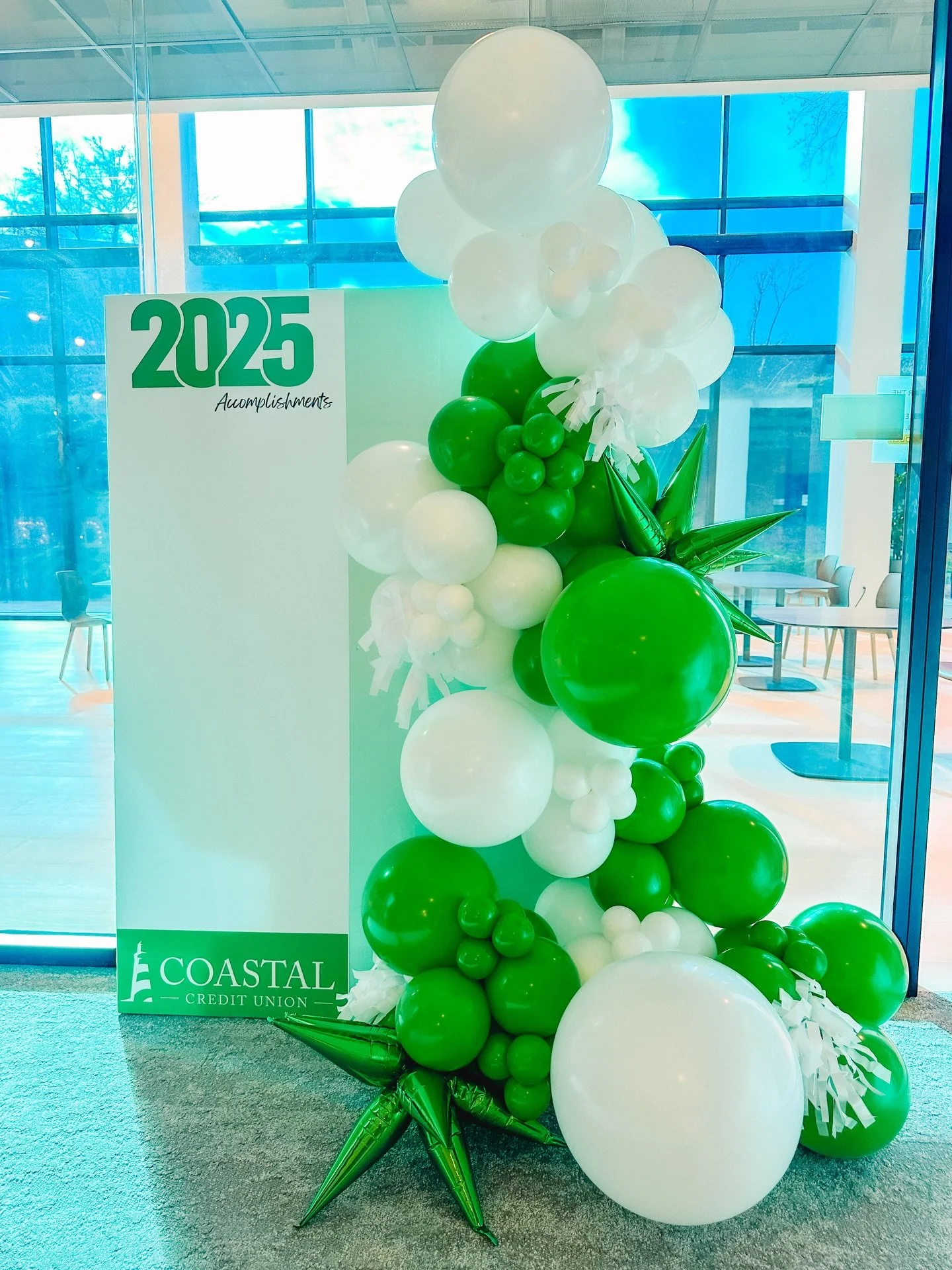 Balloon display with white and green balloons next to a white board that says '2025 Accomplishments' and features the Coastal Credit Union logo in green.