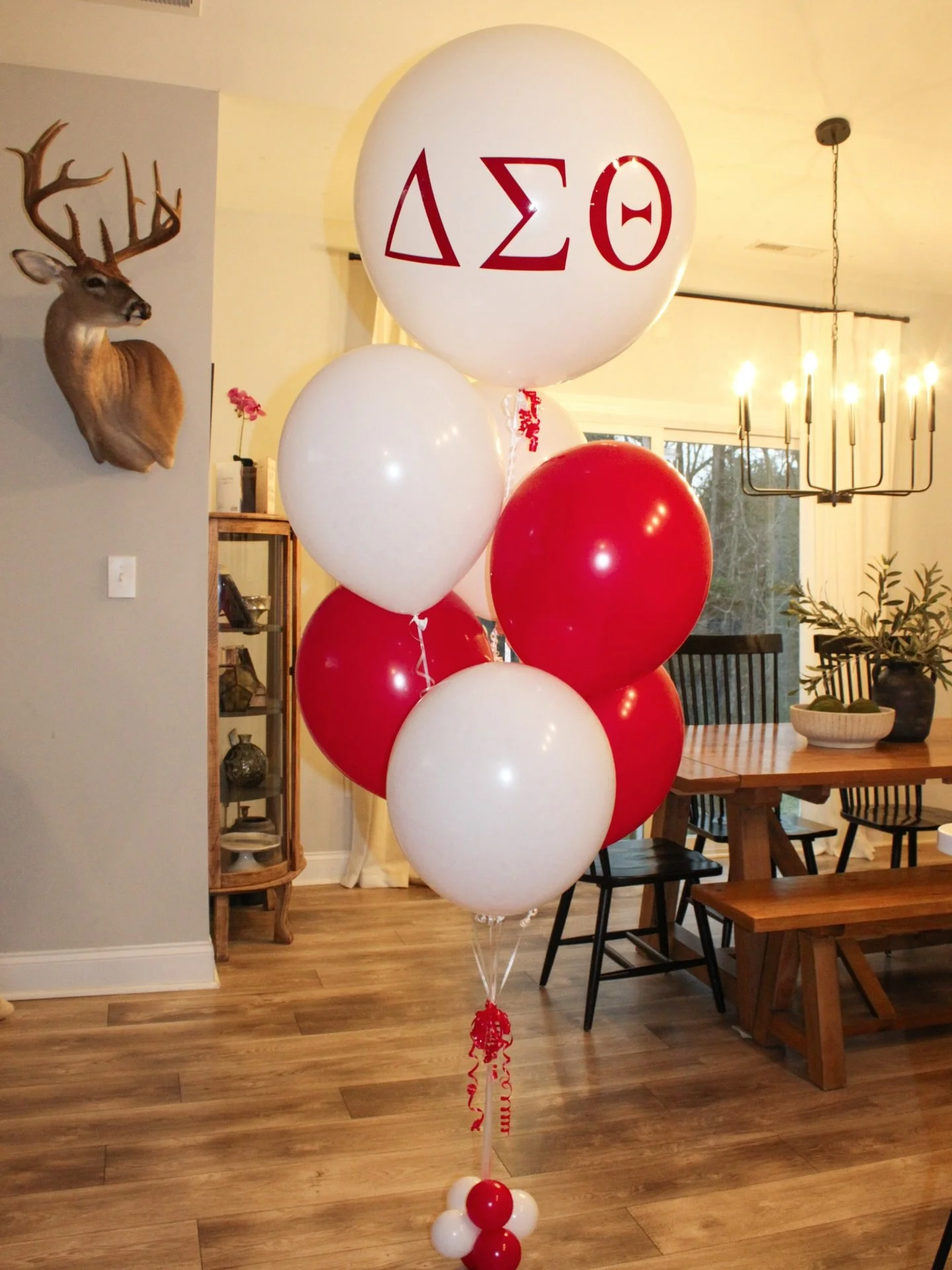 Cluster of balloons in red and white colors with Greek letters Delta Sigma Theta on the top balloon, decorating a dining area in a home.