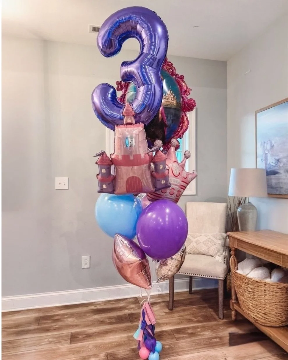 A bunch of colorful balloons, including a purple number 3 balloon and a castle-shaped balloon, arranged in a bouquet in a living room.