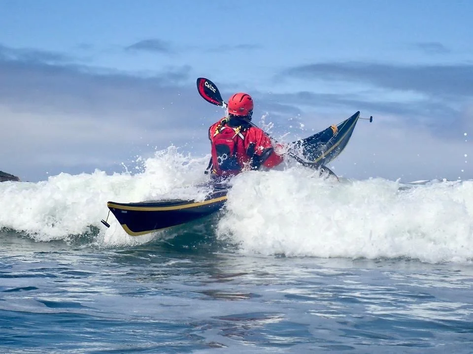 Person kayaking in rough ocean waves, wearing red helmet and jacket.