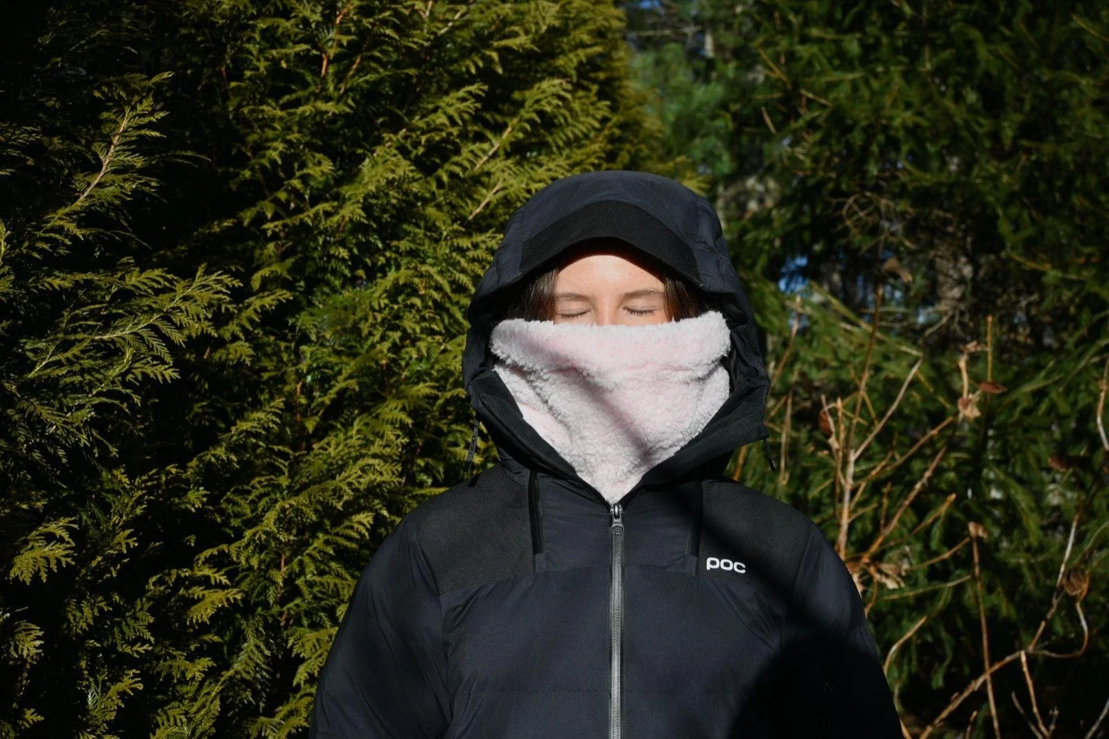 Rider in a black hooded jacket looking at the camera in the Baby Pink Sherpa neckie against green trees