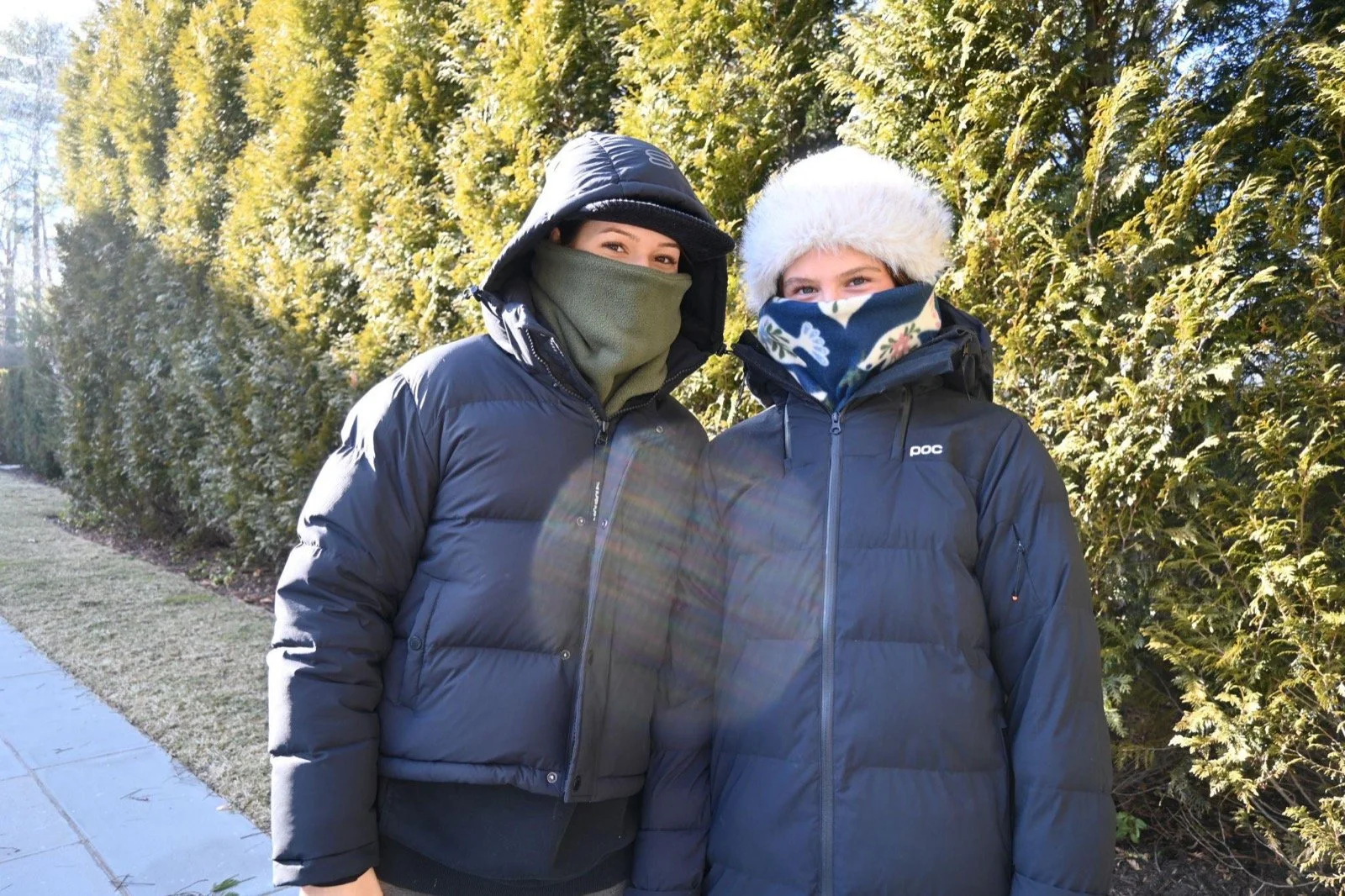Two riders in dark puffy jackets, one wearing the Army Green fleece neckie over their face