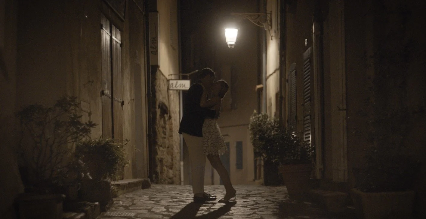 A couple dancing closely on a cobblestone street at night, illuminated by a streetlamp overhead.