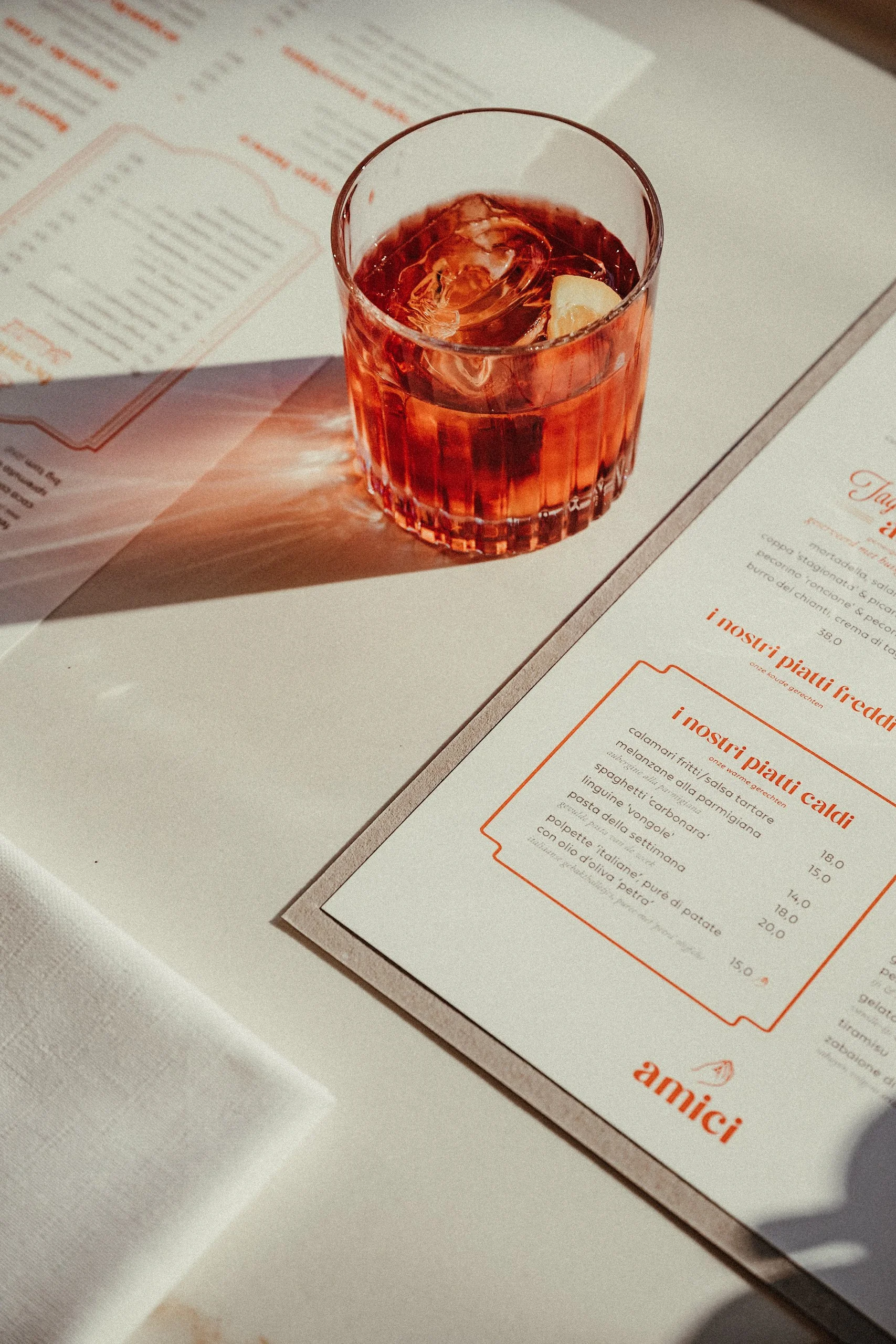 A glass of red beverage with ice cubes and a lemon wedge on a printed menu page.