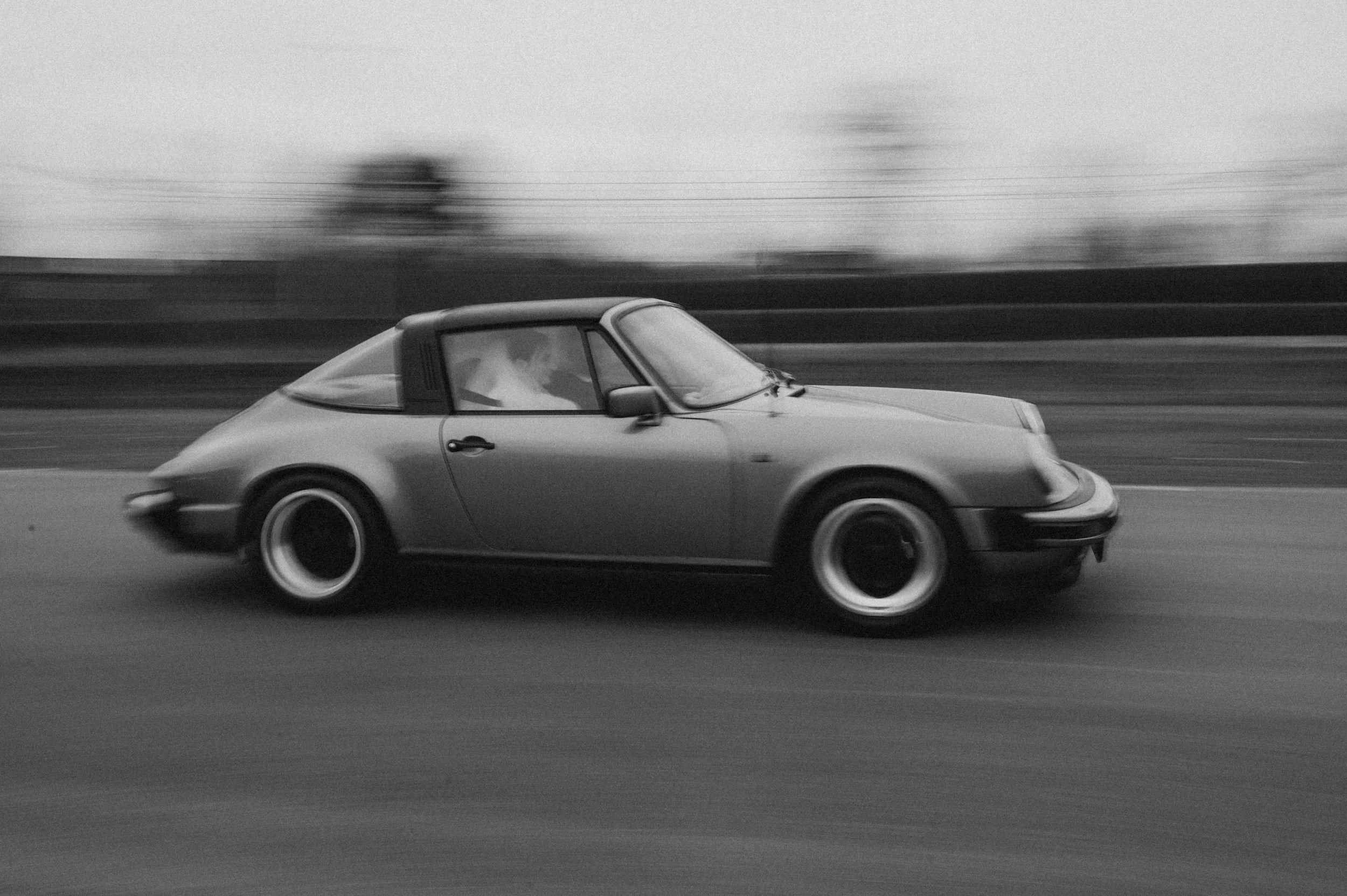 A vintage sports car, speeding on a road, with motion blur in black and white.