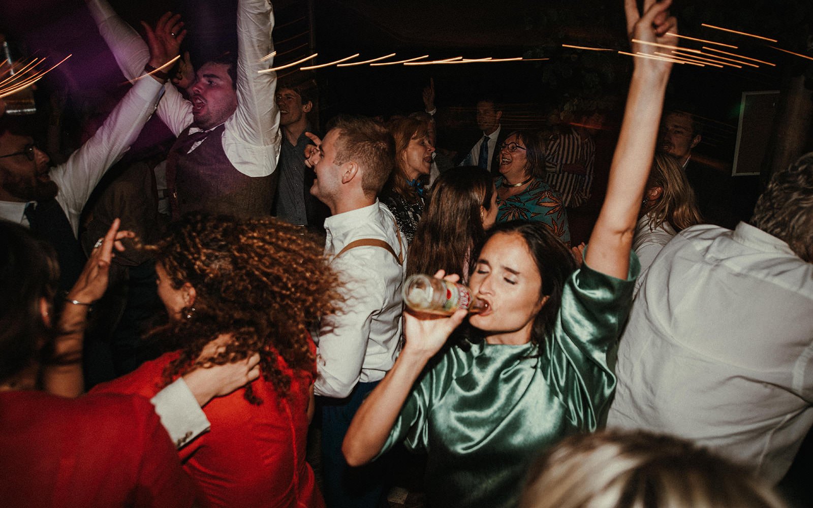 People dancing and enjoying themselves at a party or celebration, with some holding drinks and others dancing energetically.