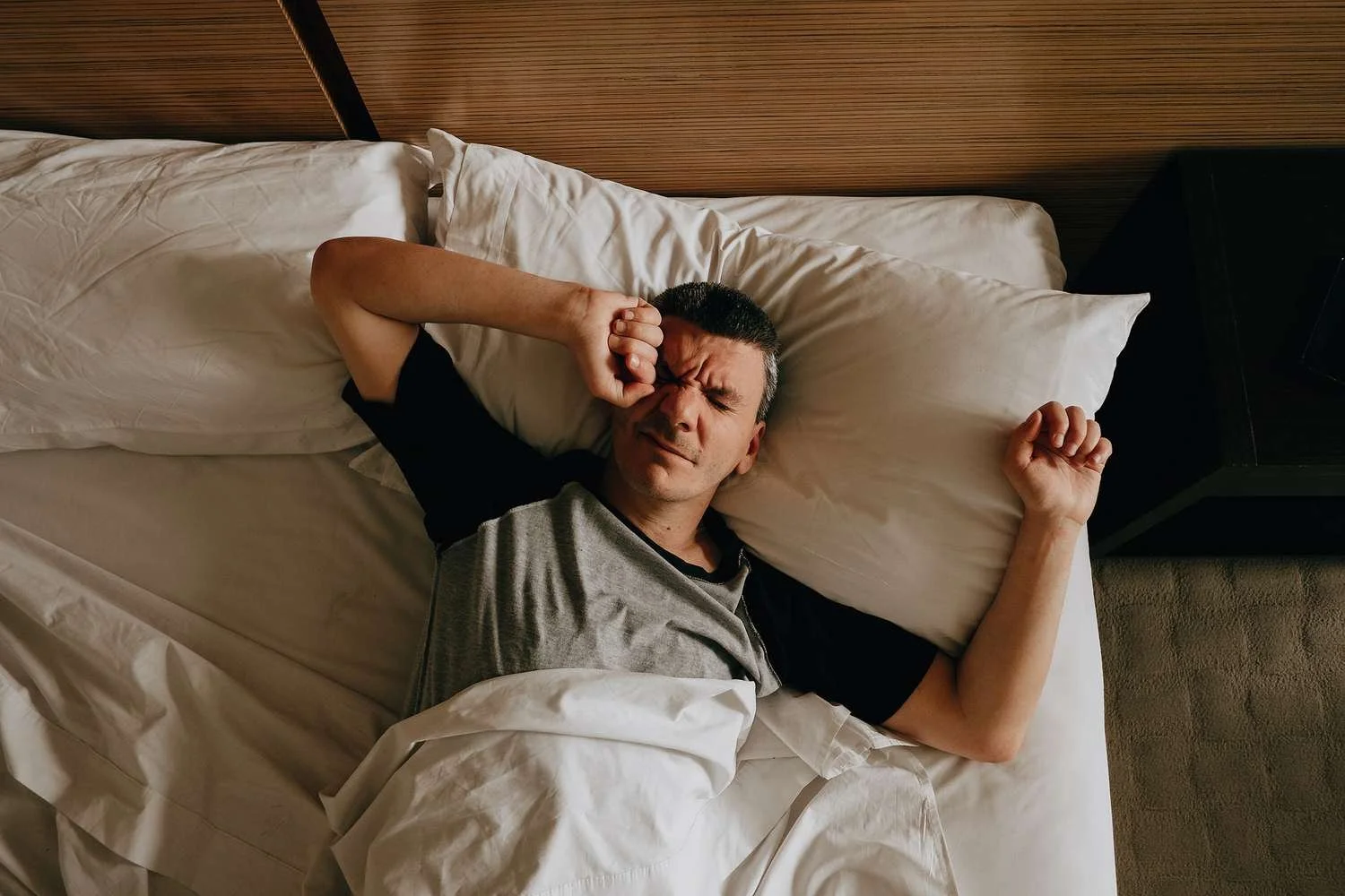 Person waking in bed looking unrested after disrupted sleep.