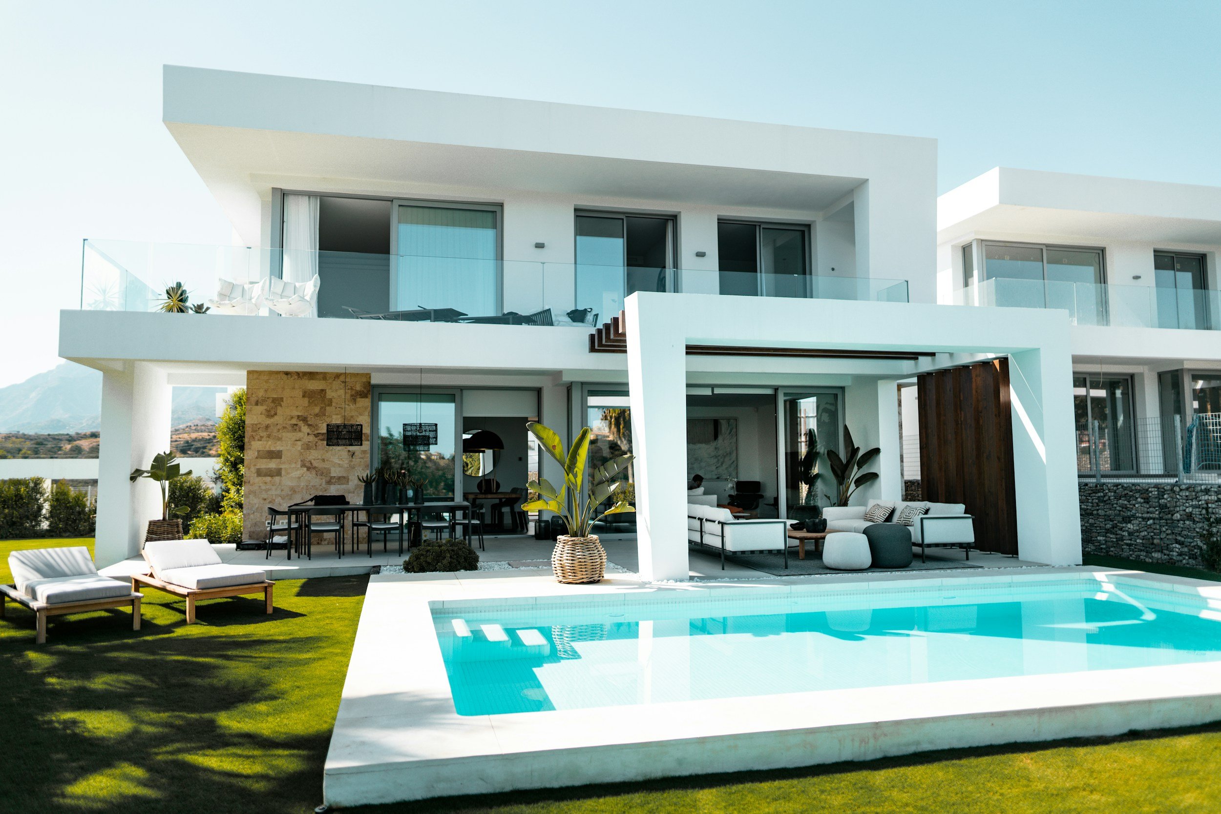 Modern white house with outdoor swimming pool, lounge chairs, green lawn, and patio furniture.