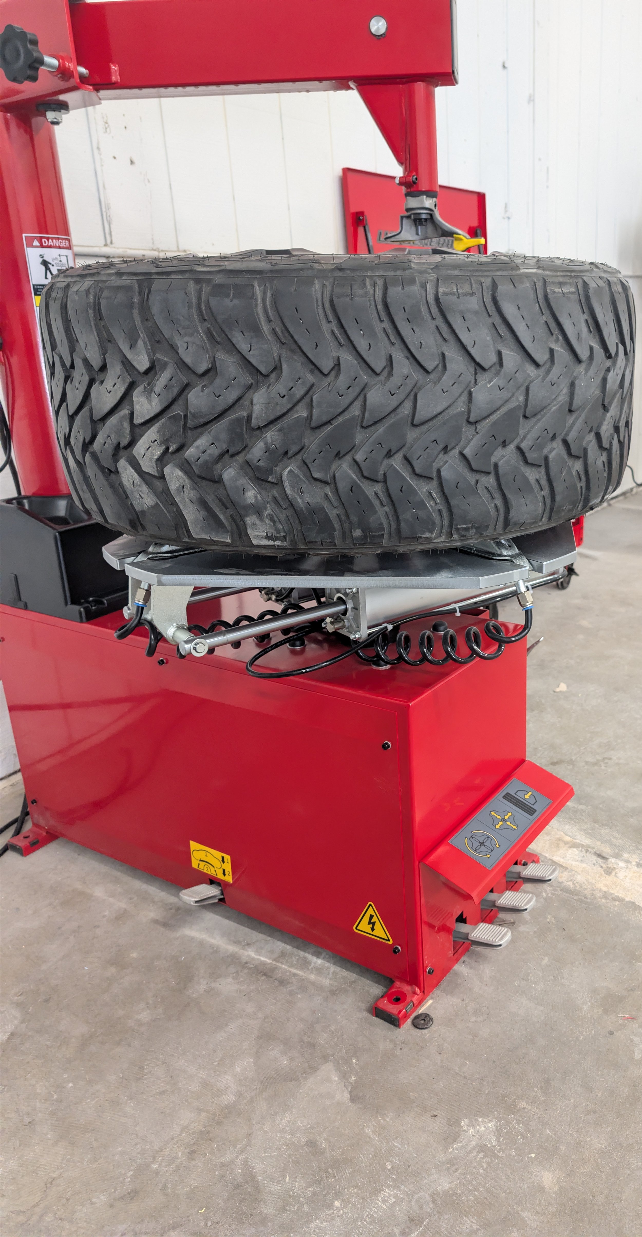 A red tire mounting machine with a large black tire on it in a workshop or garage.