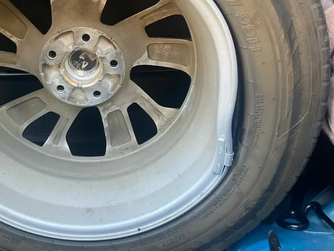 A car wheel with a rim and tire, viewed from the side. The rim is silver with multiple spokes, and the tire is black with visible tread and sidewall details.