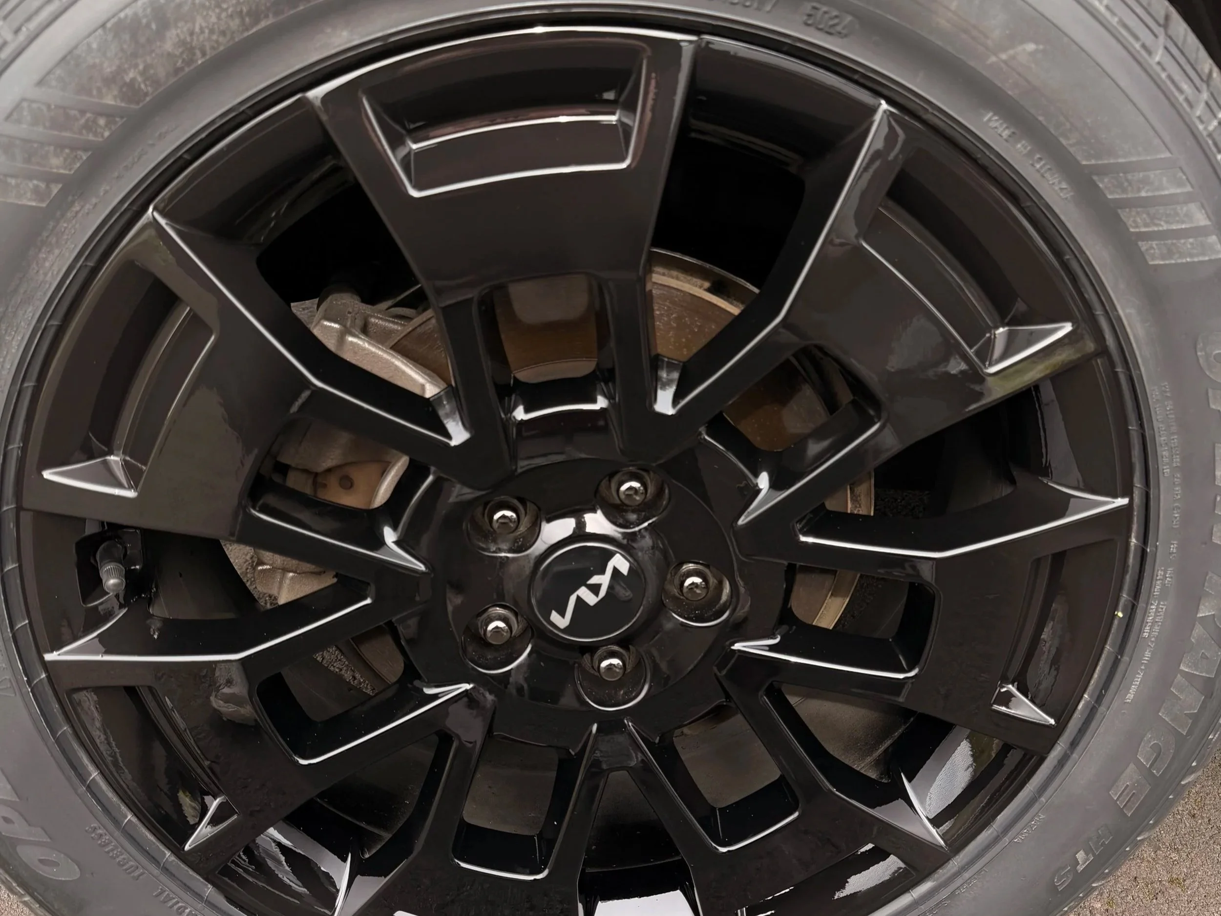 Close-up of a black alloy wheel with a logo in the center, mounted on a tire.