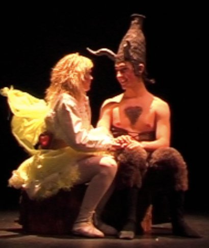 Two children in costumes sitting on a stage and holding hands, smiling at each other.