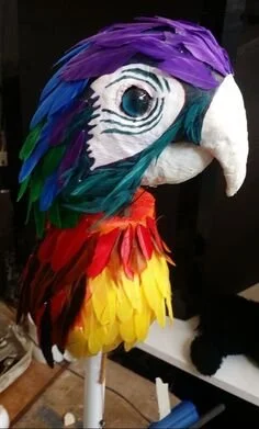 Colorful parrot-shaped mask with vibrant feathers in purple, blue, green, red, and yellow