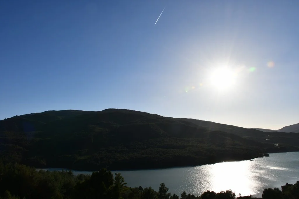Sunstar effect over a lake and mountain landscape with a faint plane contrail, Morocco