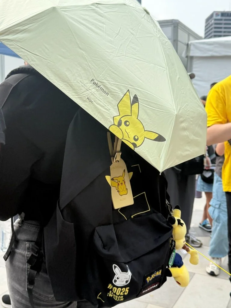 A Pokémon-branded umbrella printed with Pikachu, held over a backpack decorated with a gold Pikachu tag and matching patches
