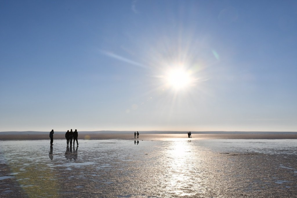 Sunstar reflected on wet salt flats with silhouetted figures, Salt Lake, Turkey