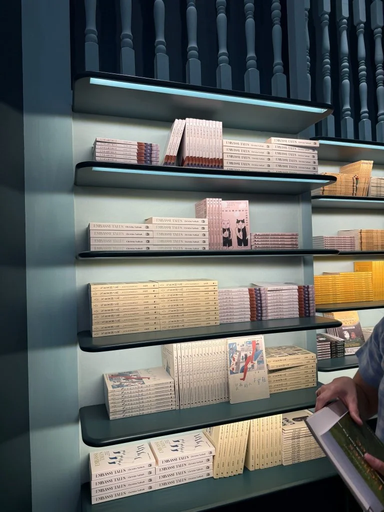 White and yellow-spined book covers displayed on a shelf at Aesop Women's Library 2026