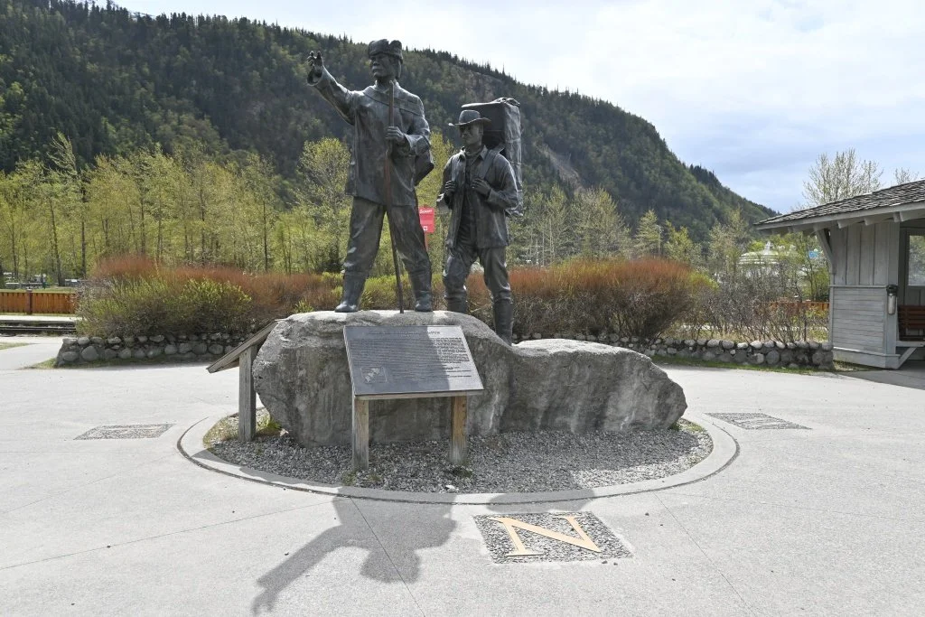 Skagway Centennial Statue featuring Tlingit packer guiding gold rush stampeder in Centennial Park