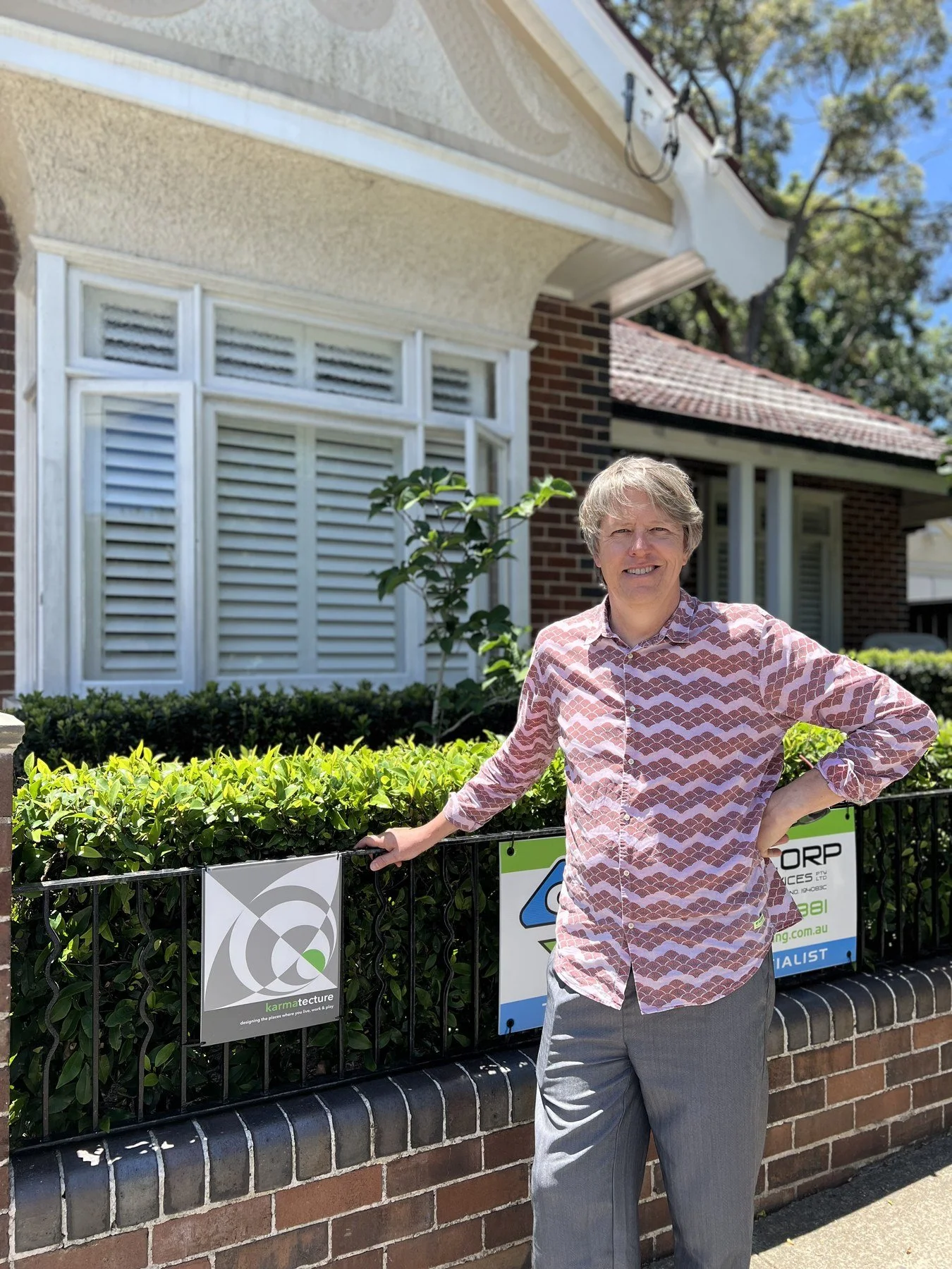 Greg Prentice, building designer and founder of Karmatecture, outside a California bungalow with a Karmatecture site sign on the fence