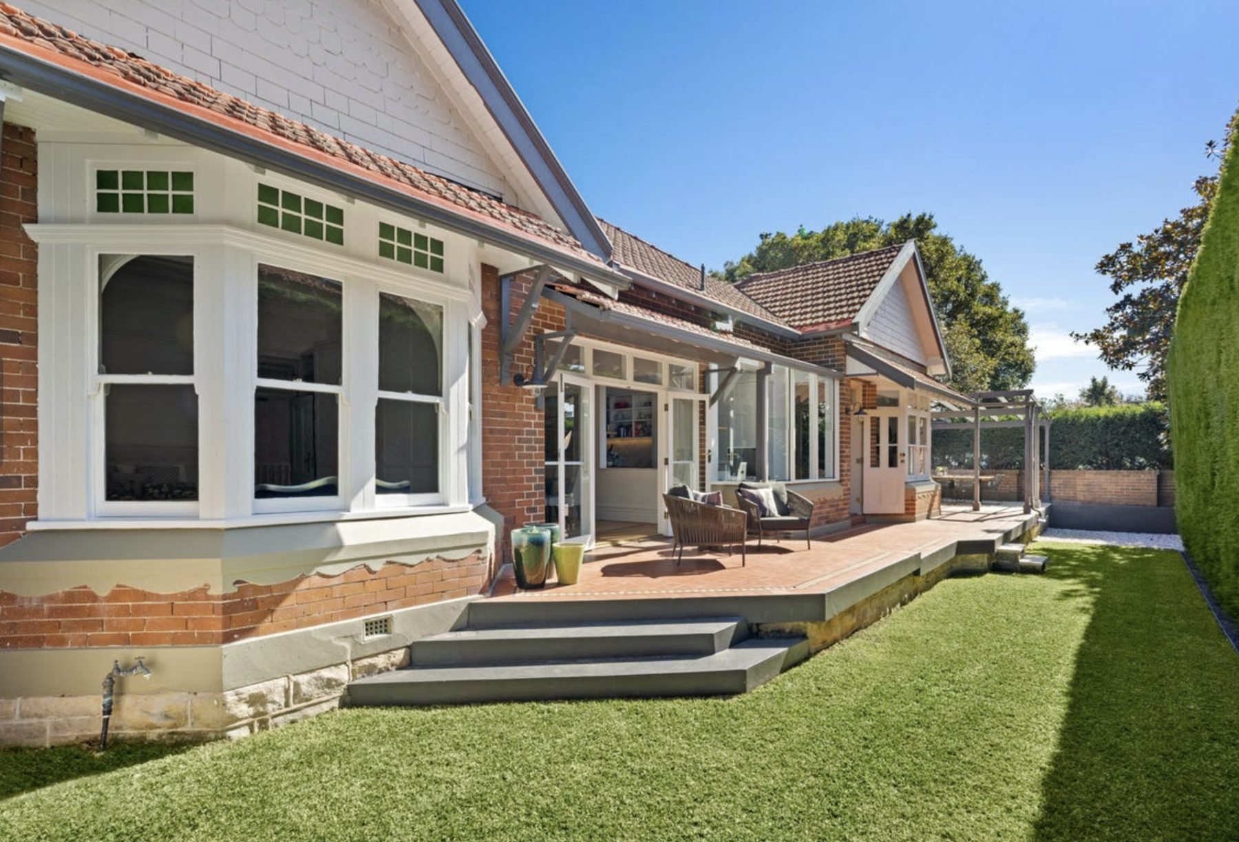 Rear elevation of a heritage brick home with leadlight windows above new landscaping and terracing
