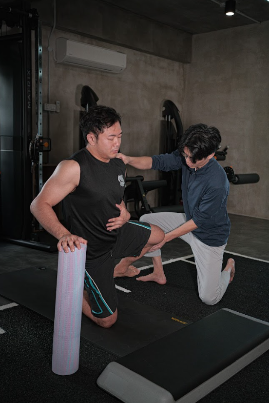 A person receiving physical therapy or training with two individuals assisting, in a gym setting with exercise equipment.