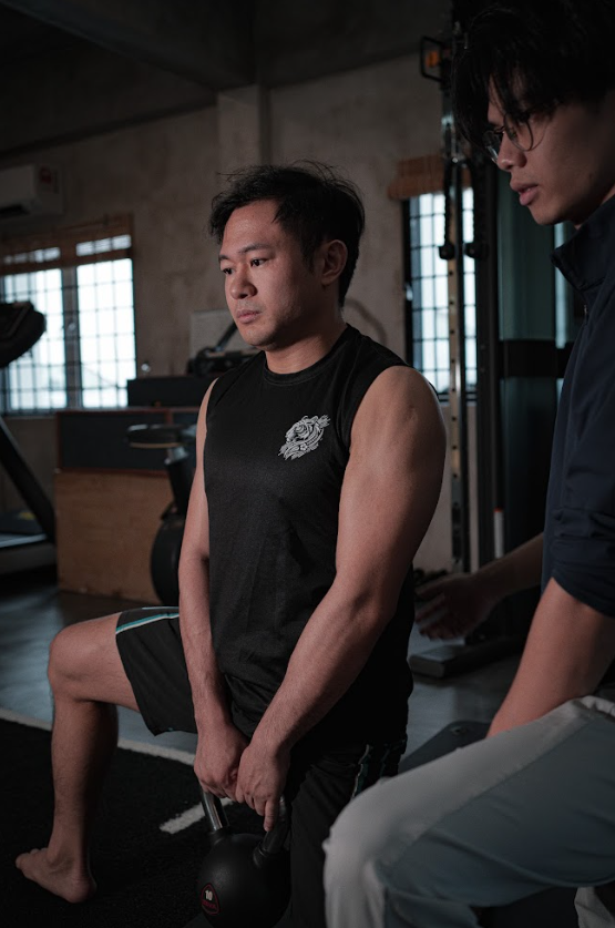 Man performing a kettlebell exercise in a gym with an instructor nearby.