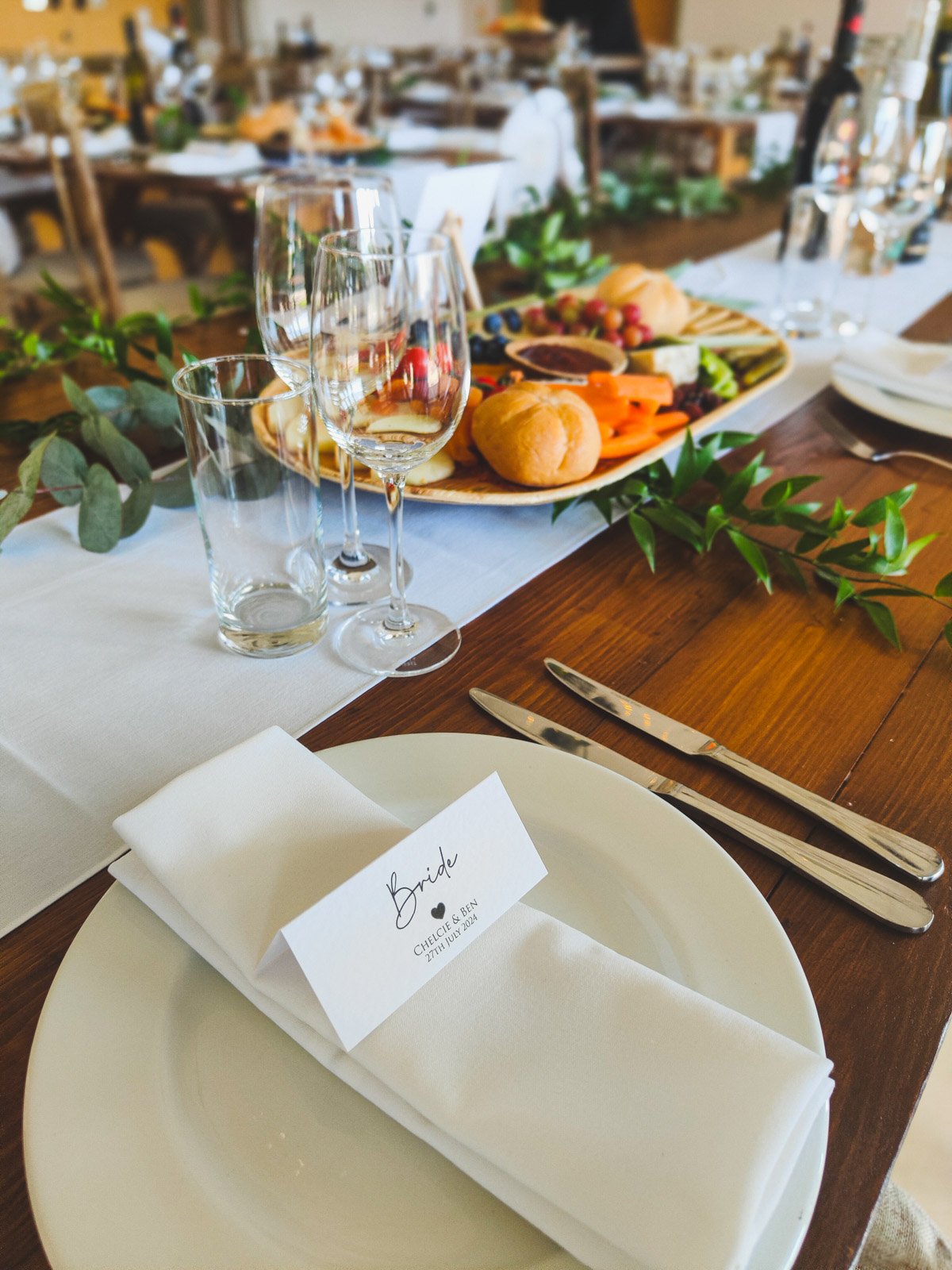 Elegant wedding table setting with place card, wine glasses and grazing platter — event photography by Wild Mind Studios