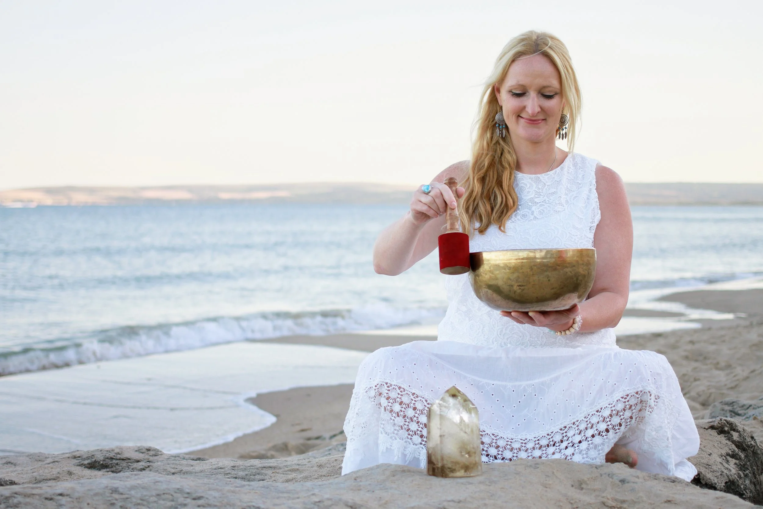 Brand photography by Wild Mind Studios Essex showing woman playing singing bowl on beach at golden hour