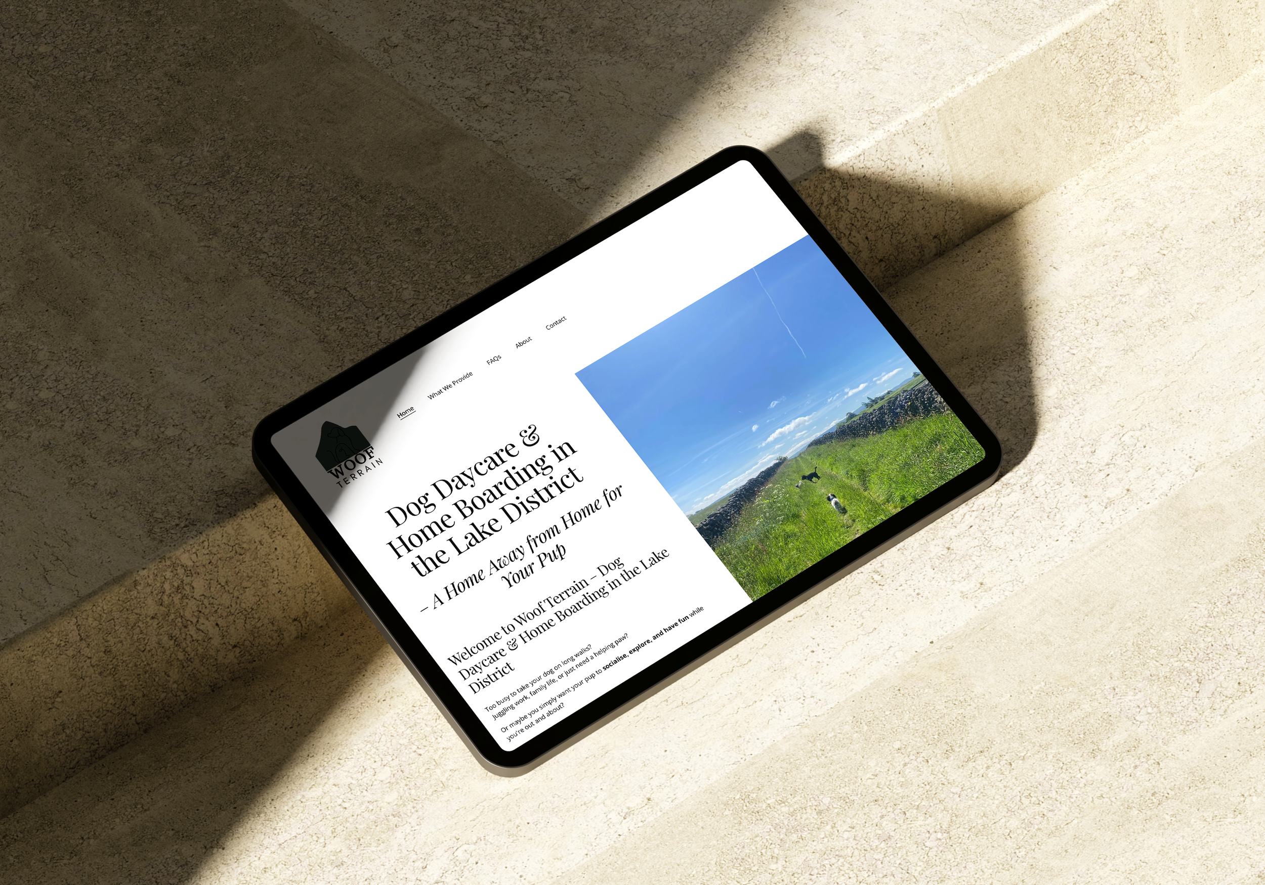 Woof Terrain website design displayed on an iPad showing the homepage with Lake District landscape photography, placed on concrete steps in warm natural light