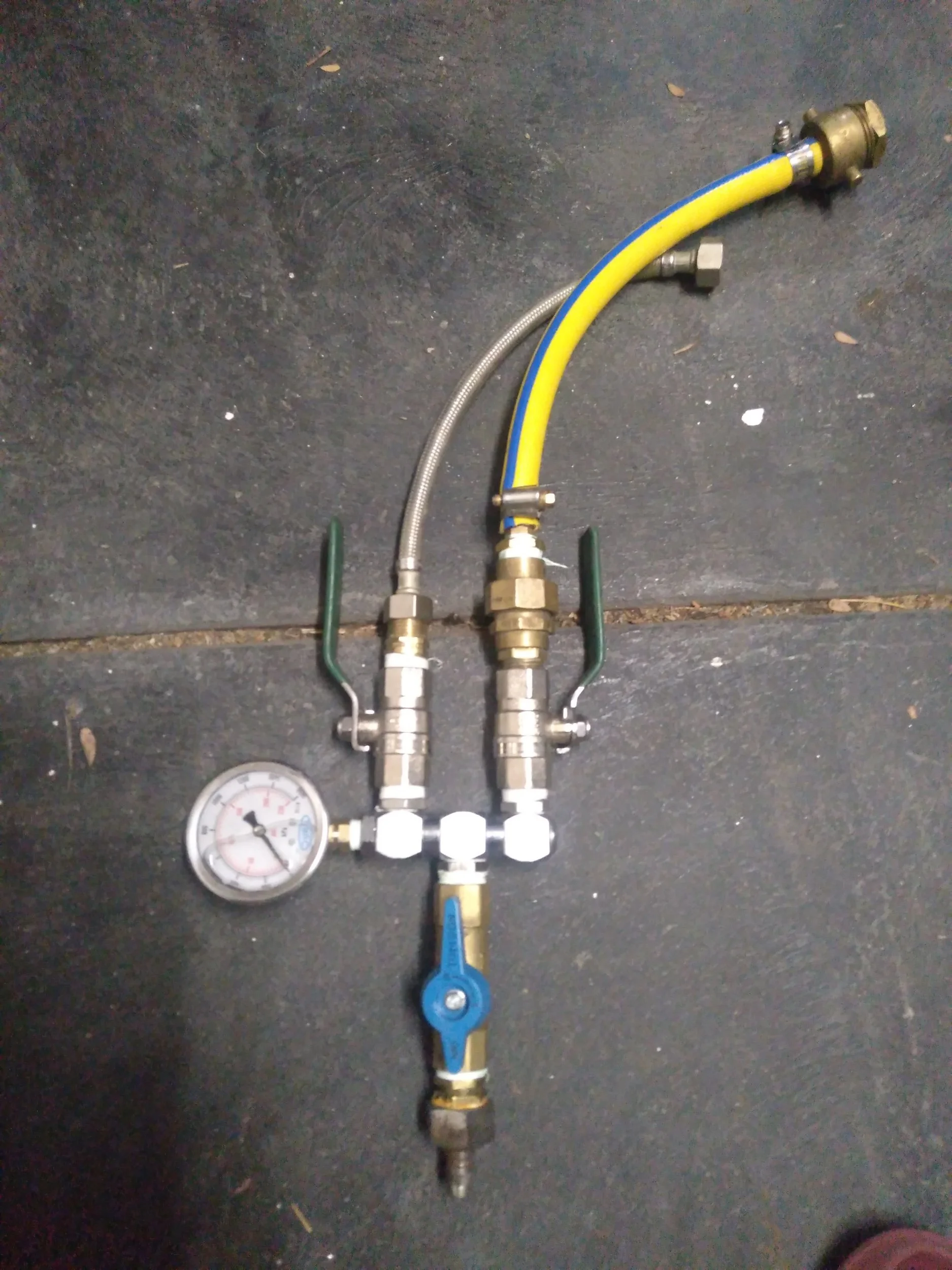 A plumbing setup with a pressure gauge, valves, hoses, and fittings on a concrete floor.