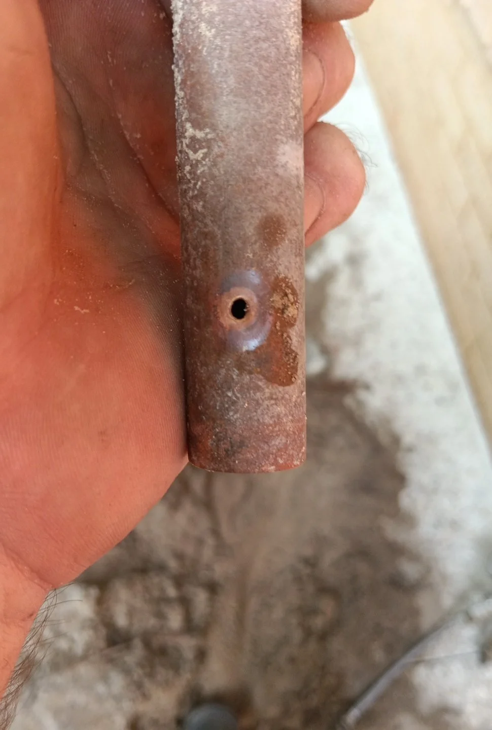 Close-up of a rusty metal pipe with a small hole near its center, held in a person's hand.