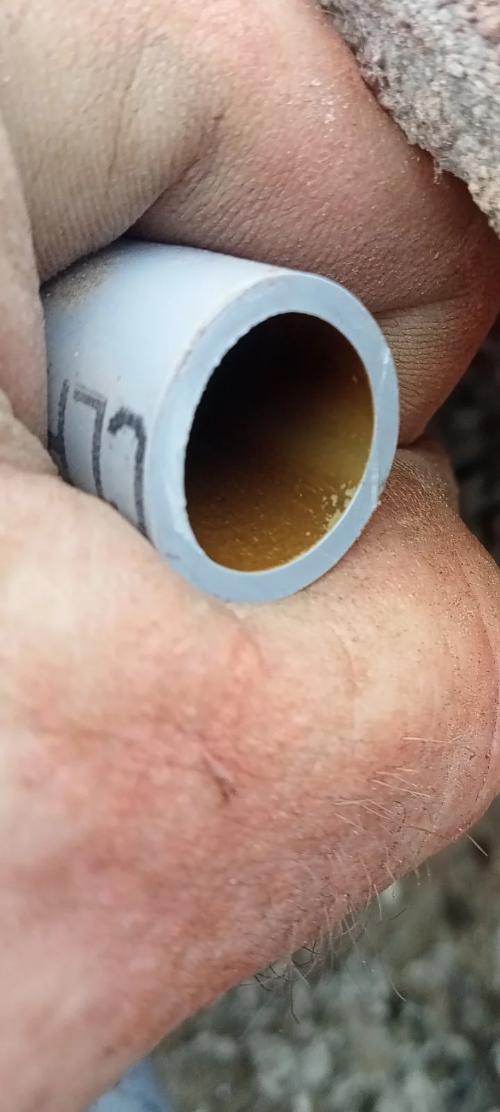 Close-up of a person's hand holding a small pipe, with dirt and rough skin visible.