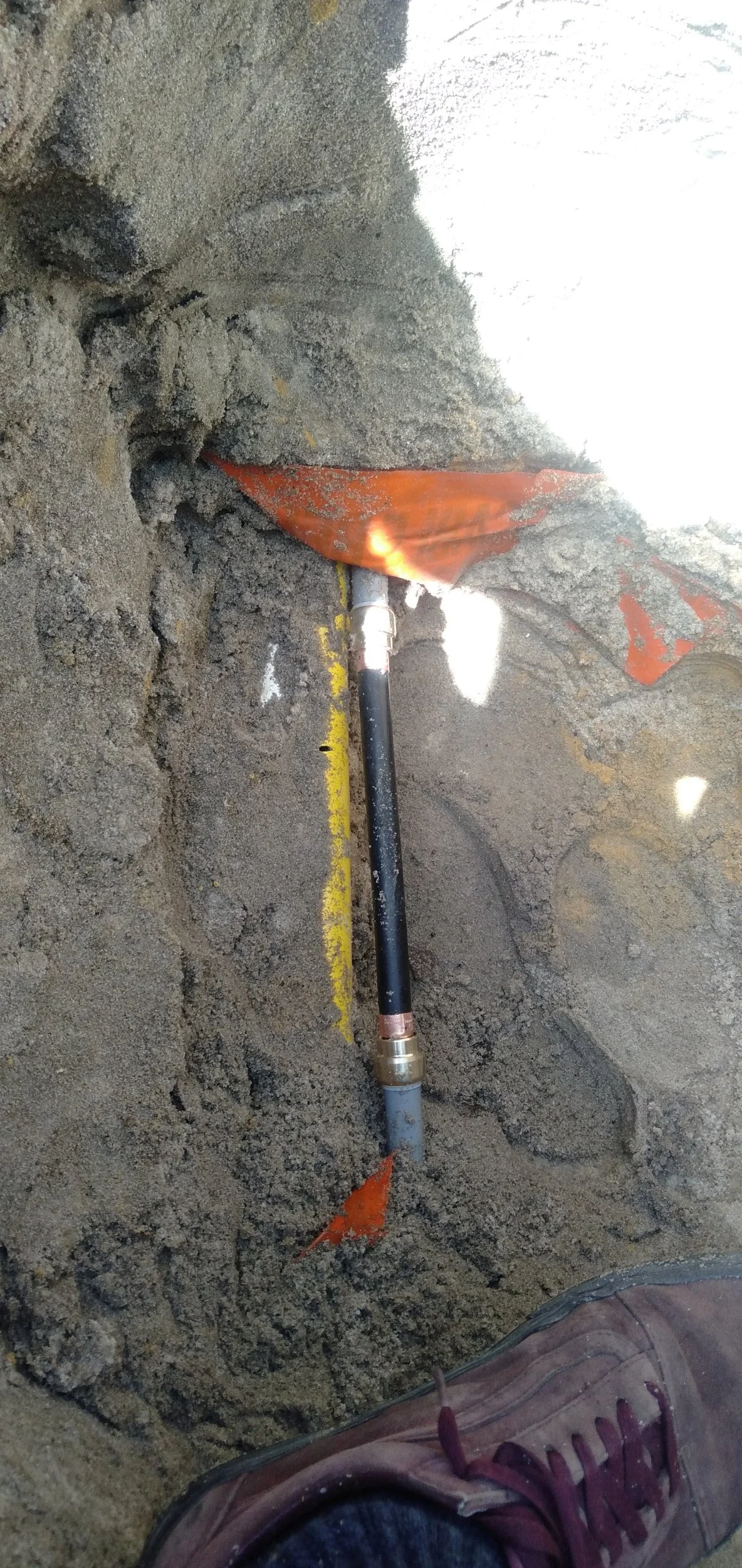 Oil or gas pipeline being repaired underground, with a pipe laying in a trench filled with dirt and gravel, and an orange safety flag nearby.