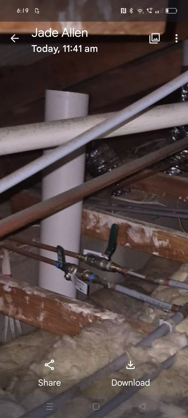 Construction site with exposed pipes, plumbing fixtures, and insulation in a ceiling framework.