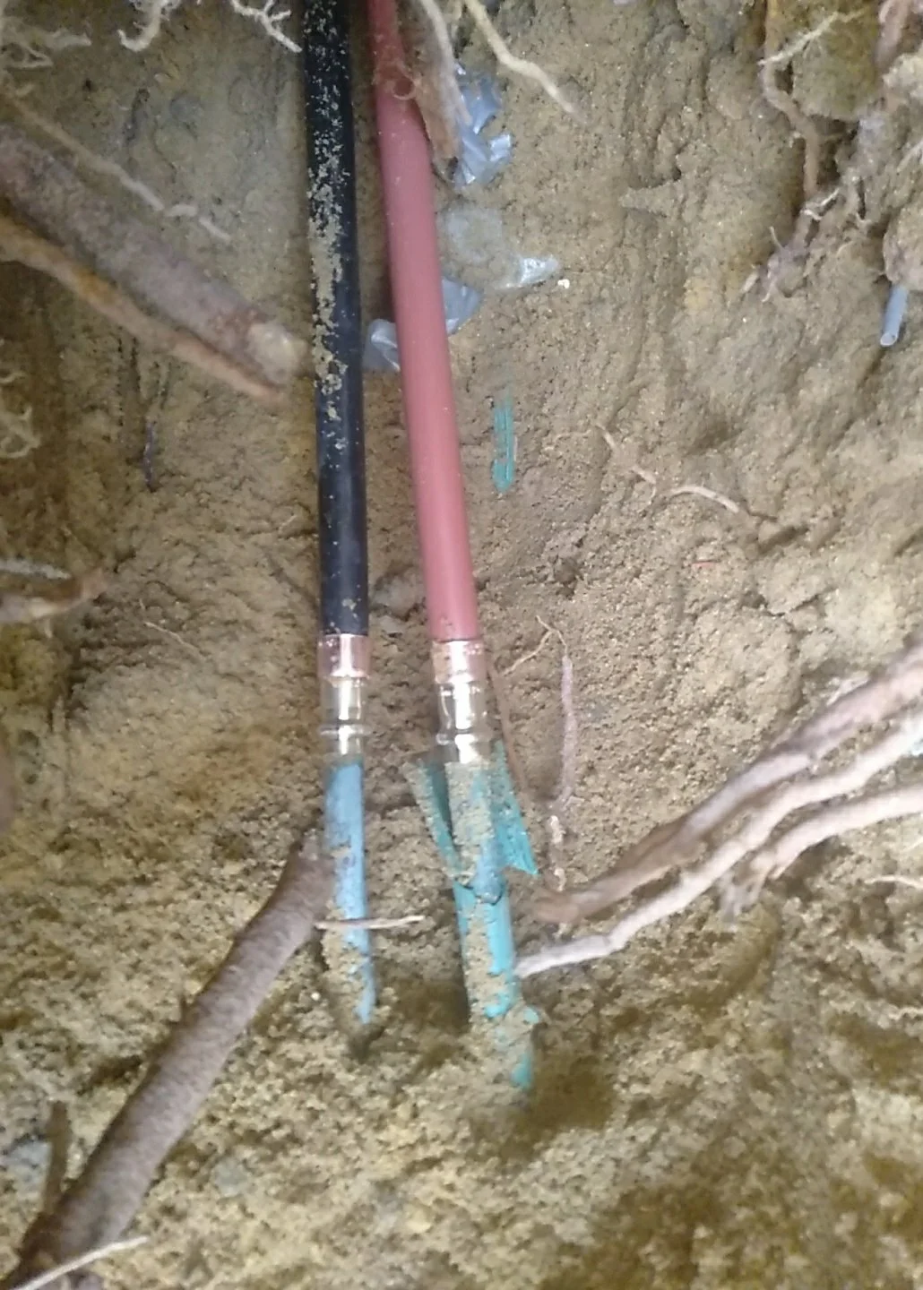 Close-up view of plumbing pipes, one black and one pink, embedded in a hole in the ground.