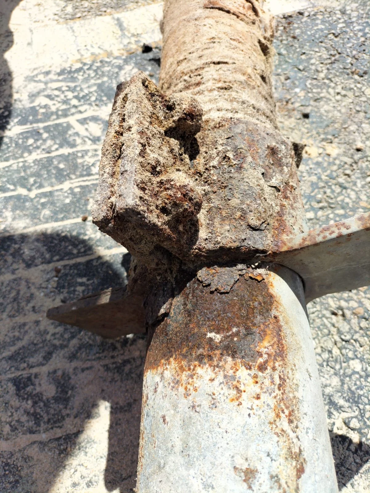 Close-up of a rusty, corroded metal object with a bolt and rusted metal components, on a gravel surface.
