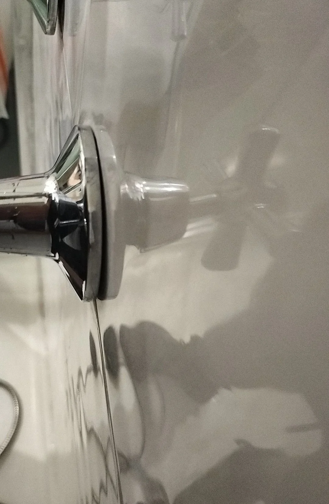 Close-up of a shiny chrome faucet on a white bathroom sink with a reflection of the person's hand holding a camera or phone.