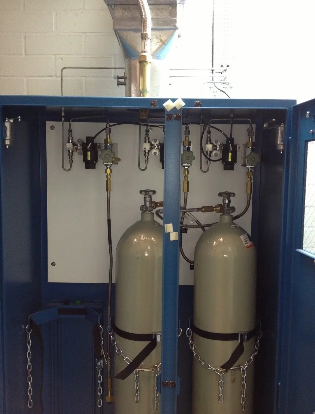 Two large oxygen tanks inside a blue metal cabinet connected to gauges and valves.