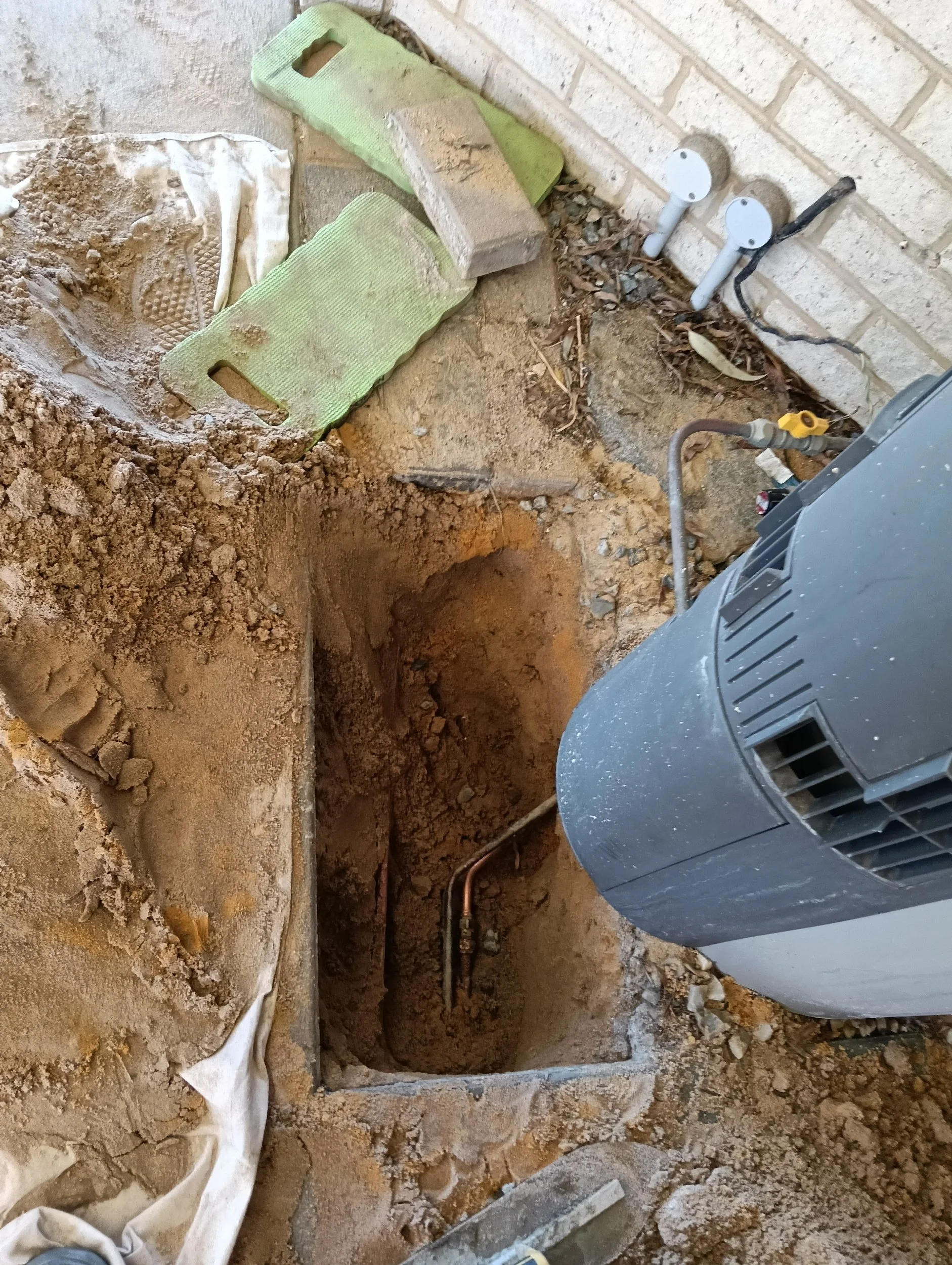An open excavated hole in the ground with plumbing and construction tools around, including a green foam float and a gray piece of equipment.