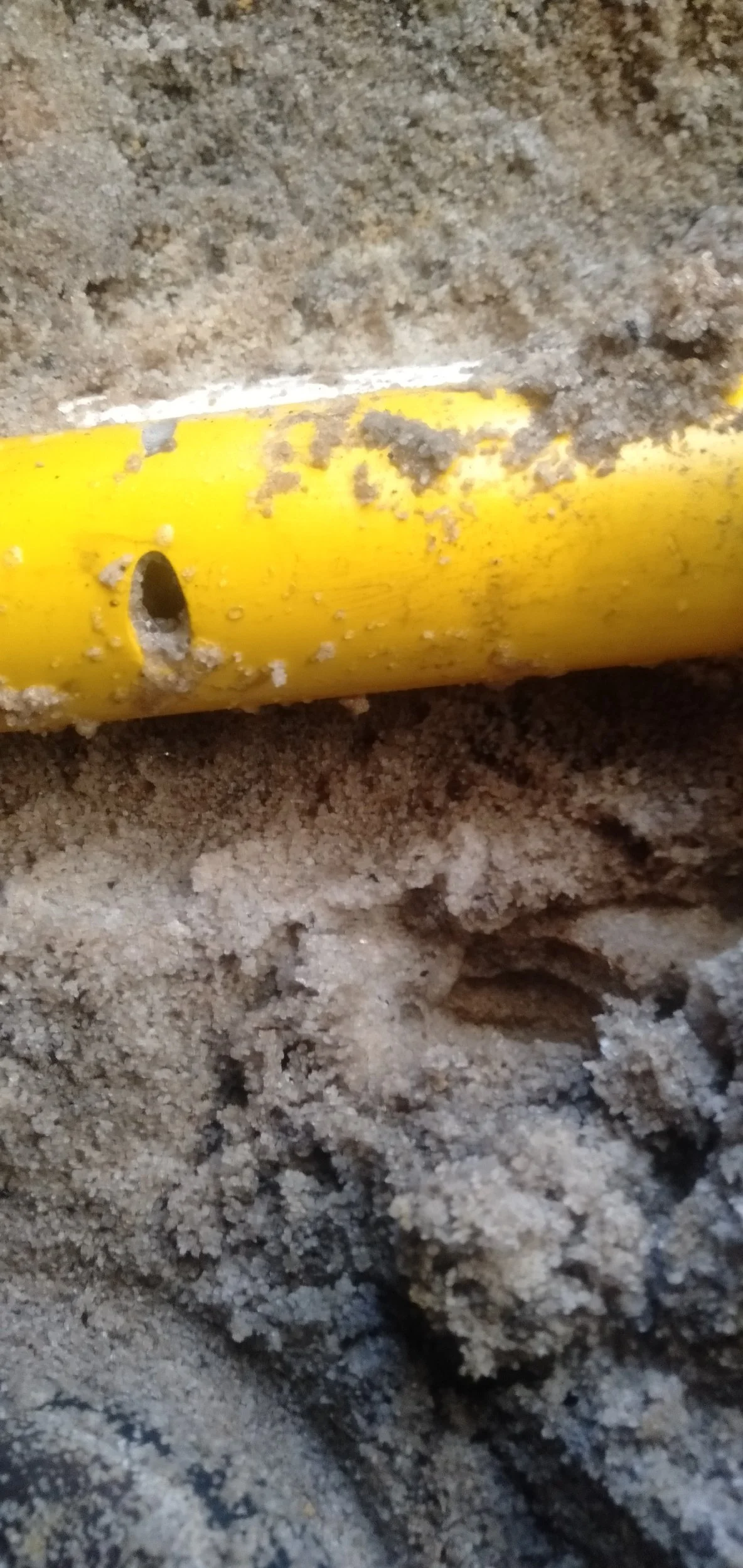Close-up of a yellow plastic object partially buried in sandy soil, with some dirt and sand covering it.