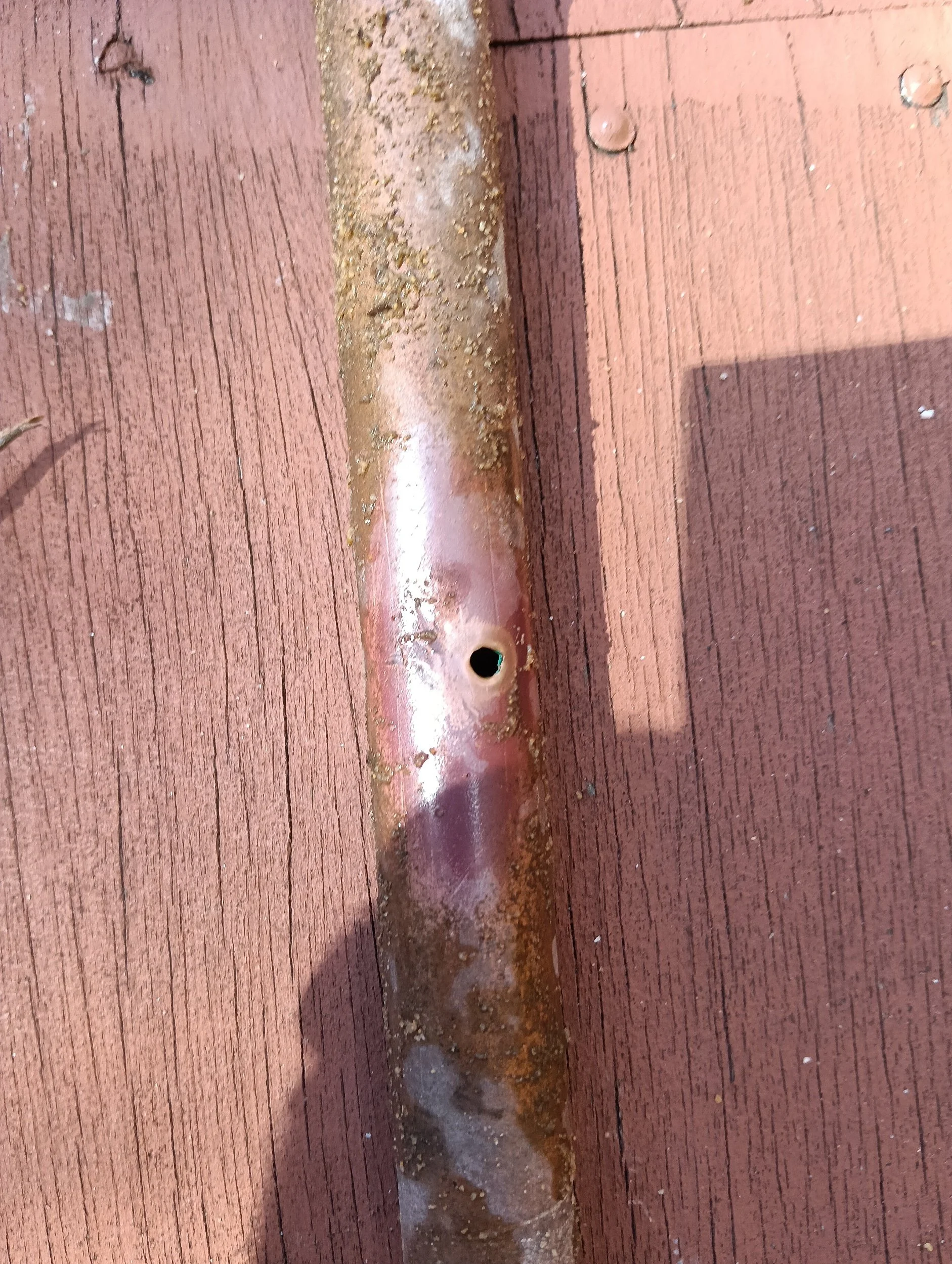 Rusty metal pipe with a small hole, placed on a red wooden surface with grooves.