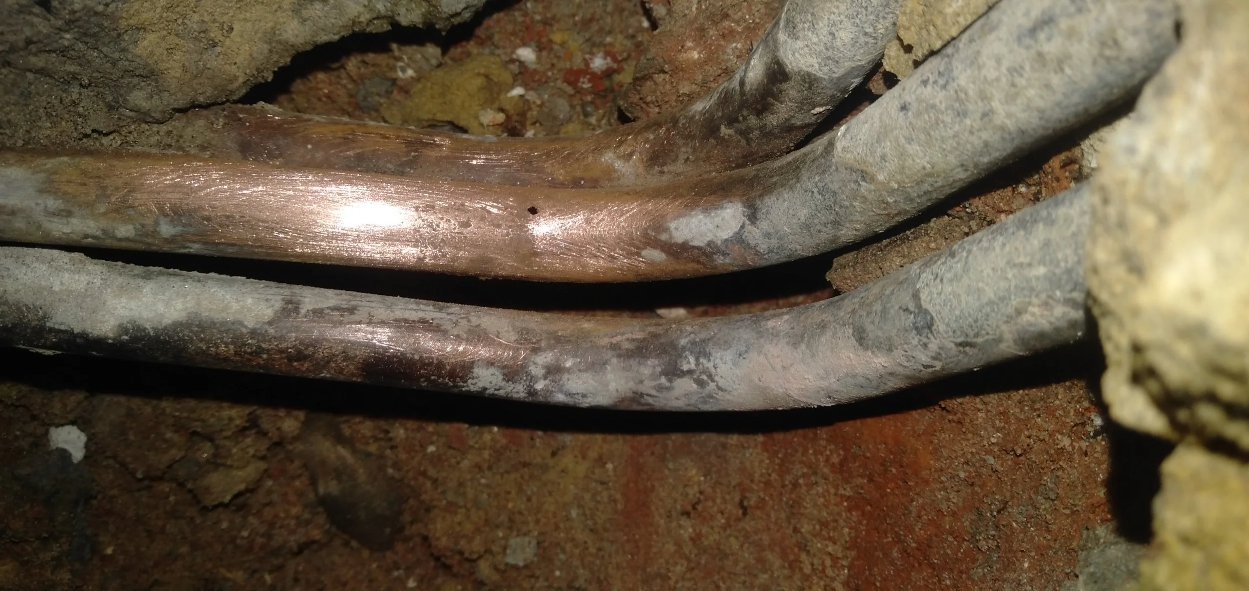 Close-up of copper pipes in a wall, showing signs of corrosion.
