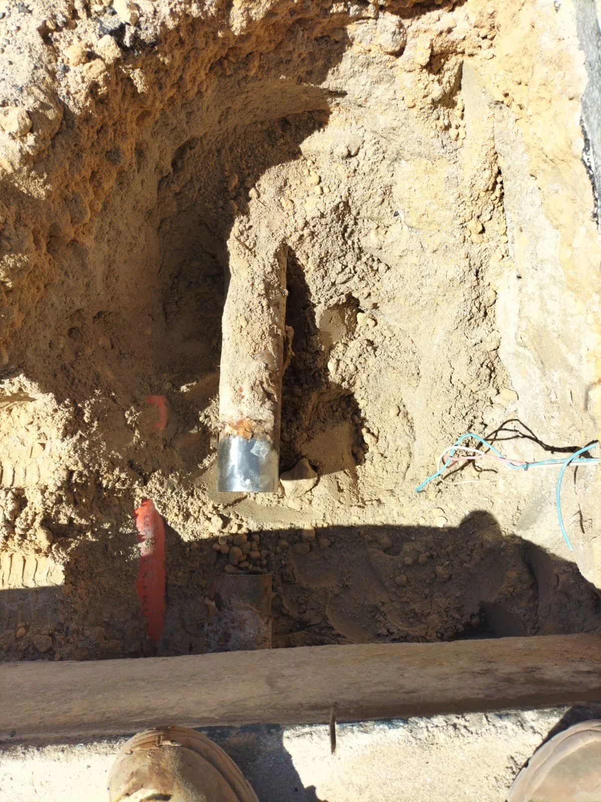 Underground utility installation with metal pipe and electrical wiring in a dug trench.