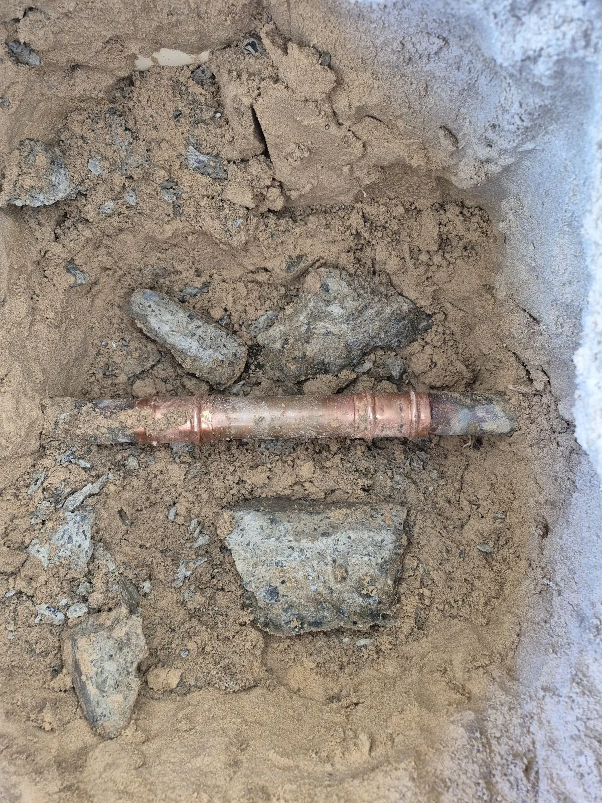 A copper pipe lying in a dirt hole surrounded by rocks.