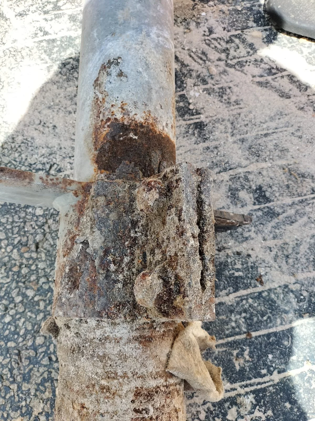 Close-up of a rusty metal pipe and bracket on a gravel surface.