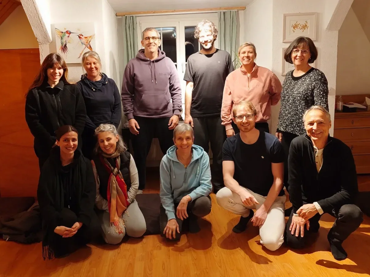 Abschlussfoto von zehn Absolventen der Chakra Ausbildung in einem Wohnzimmer, einige sitzen auf dem Boden, andere stehen, alle lächeln für die Kamera.