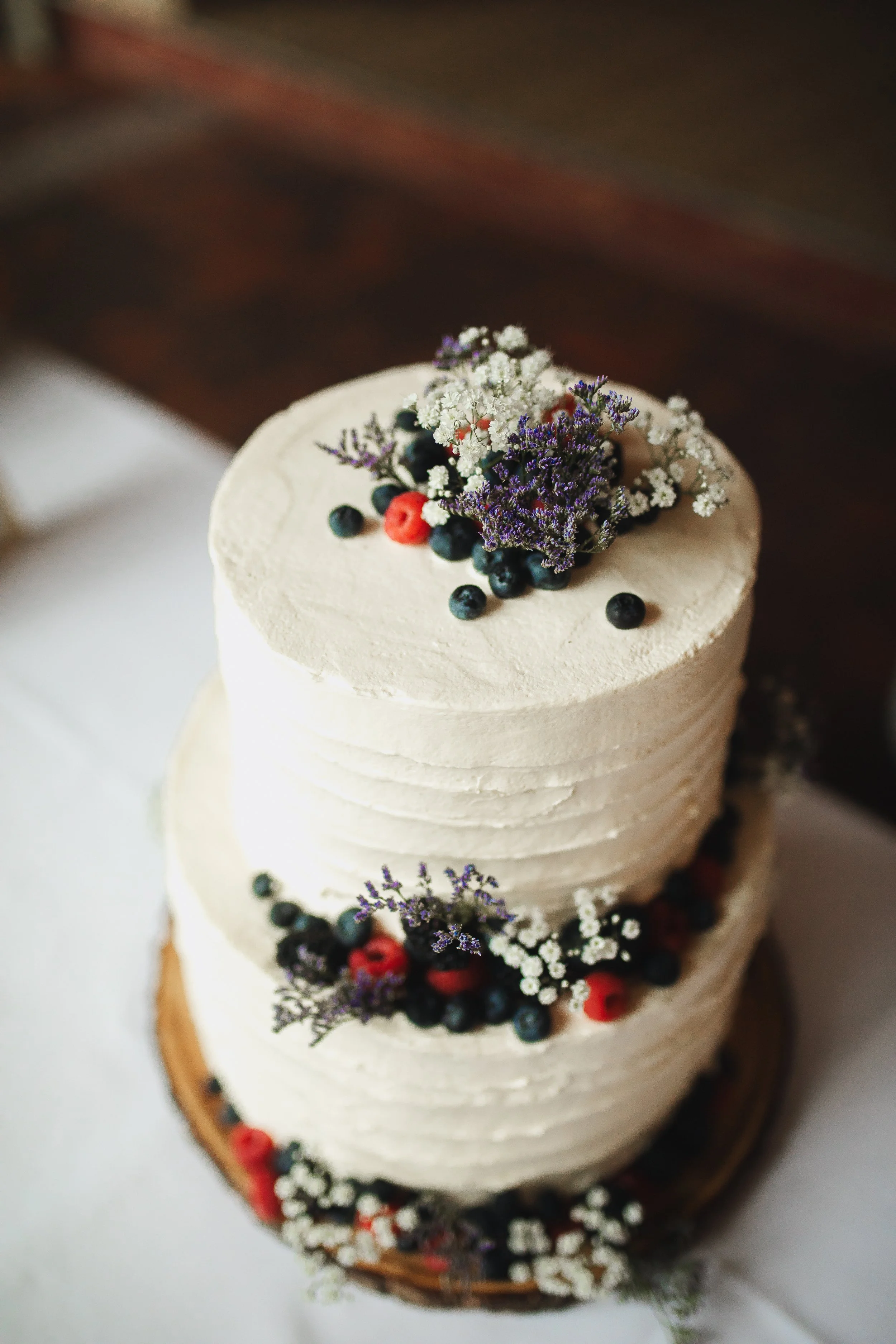 Eine festliche Torte mit Beeren und Blumen als Dekoration, umgeben von warmen Lichterglanz, auf einer eleganten Unterlage präsentiert.