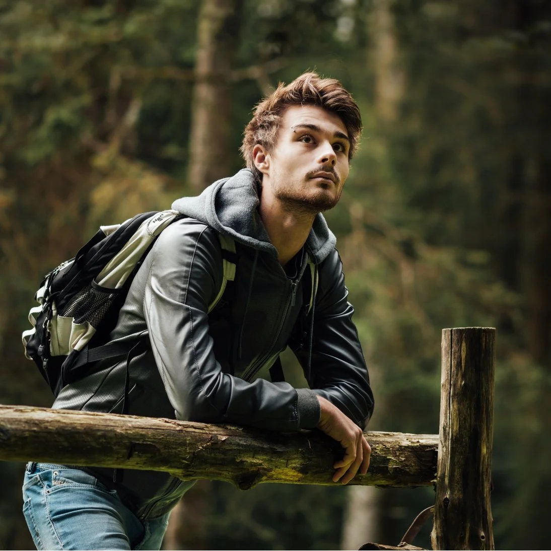 Thoughtful young man leaning on fence in nature