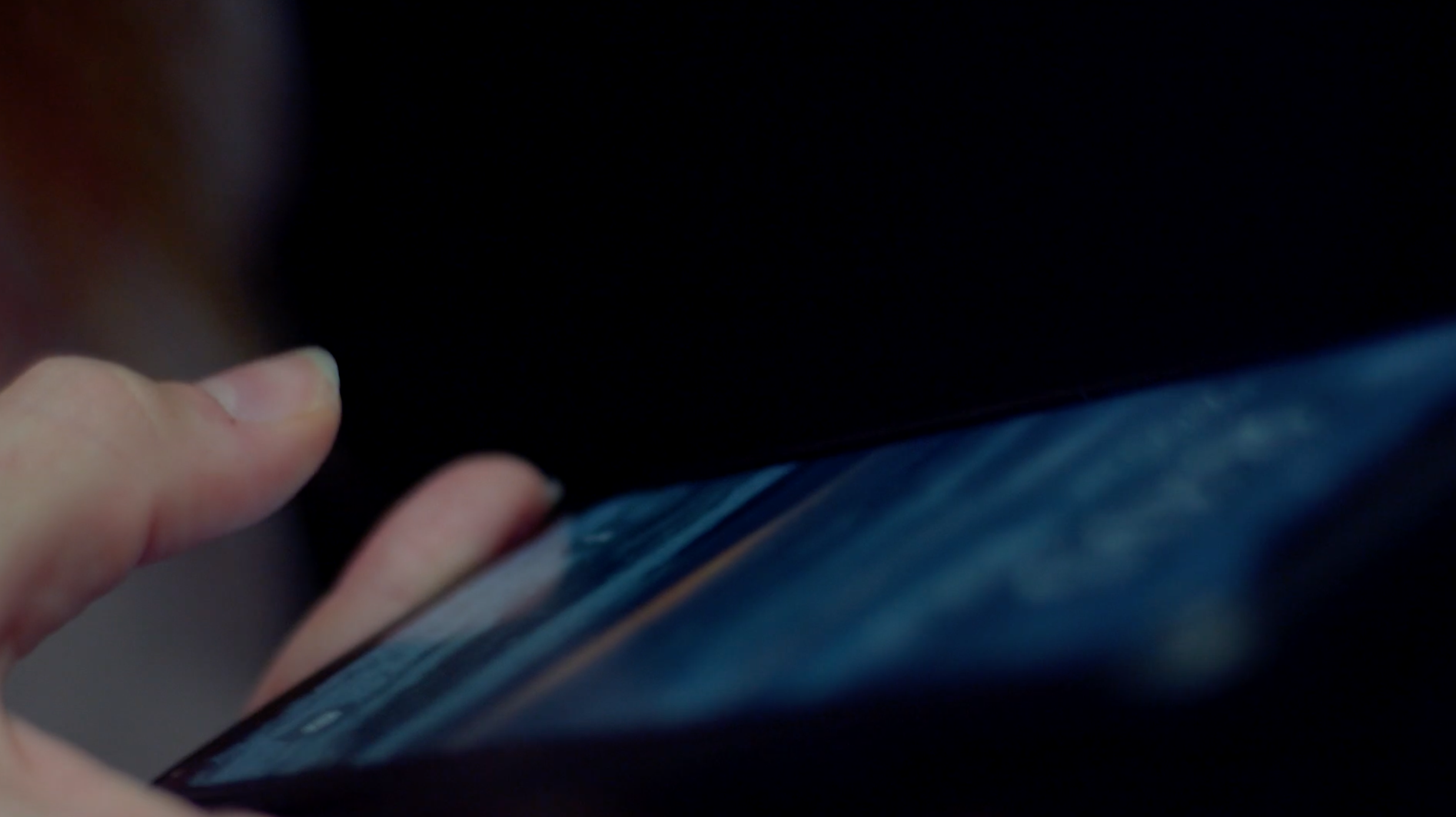 Close-up of a person holding and using a smartphone in a dark environment.