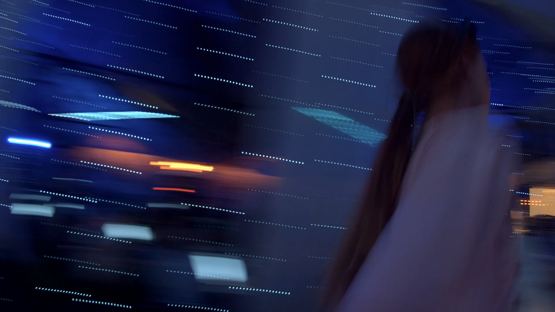 Blurred image of a person with long hair under blue and orange lights, creating a motion effect.